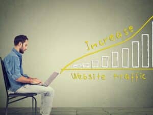 A man sitting on a chair with a laptop and a graph, learning how to get more traffic to his fitness website for free.